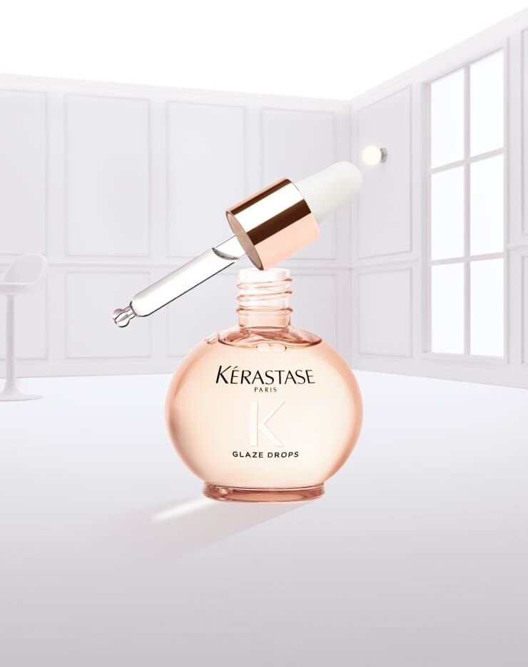 Eine Flasche Kerastase Glaze Drops mit einer tropfenden Pipette, vor einem neutralen Hintergrund.