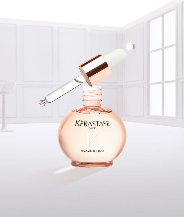 Eine Flasche Kerastase Glaze Drops mit einer tropfenden Pipette, vor einem neutralen Hintergrund.