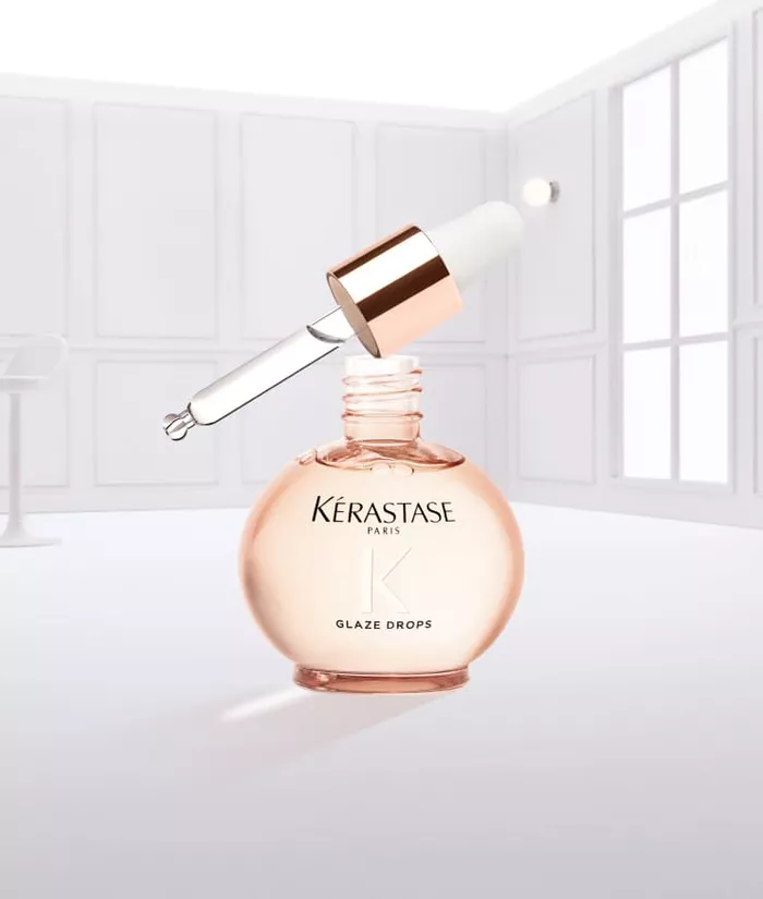 Eine Flasche Kerastase Glaze Drops mit einer tropfenden Pipette, vor einem neutralen Hintergrund.