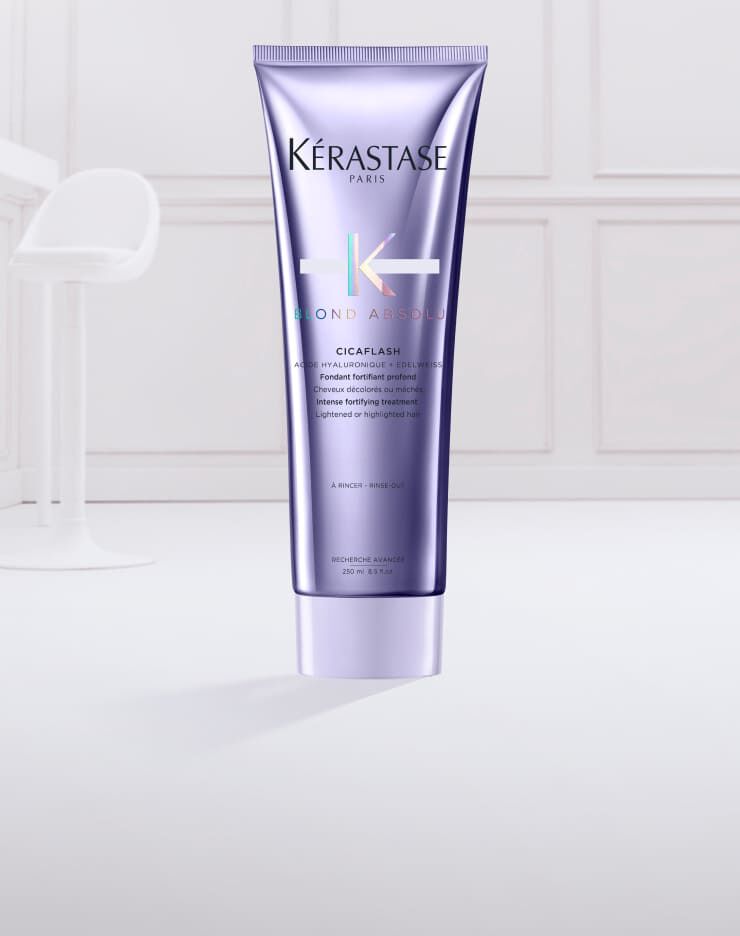 Ein lila Tubus von Kerastase „Blond Absolu“ Cicaflash mit einer cremigen, blauen Haarpflegeformulierung, die aus der geoffneten Tube herausquillt.