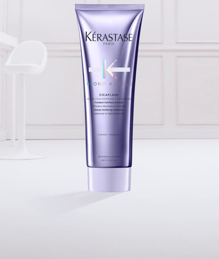 Ein lila Tubus von Kerastase „Blond Absolu“ Cicaflash mit einer cremigen, blauen Haarpflegeformulierung, die aus der geoffneten Tube herausquillt.