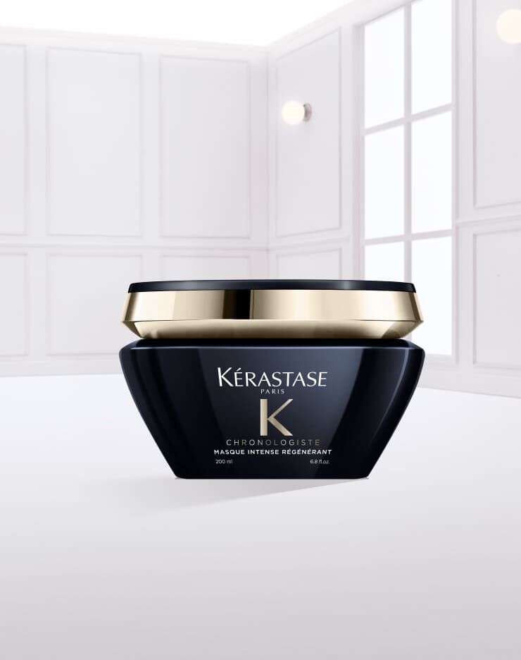 Ein schwarzer Kosmetikbehalter von Kerastase mit goldener Kappe, gefullt mit einer weißen Haarcreme, steht auf einer glatten, weißen Oberflache.