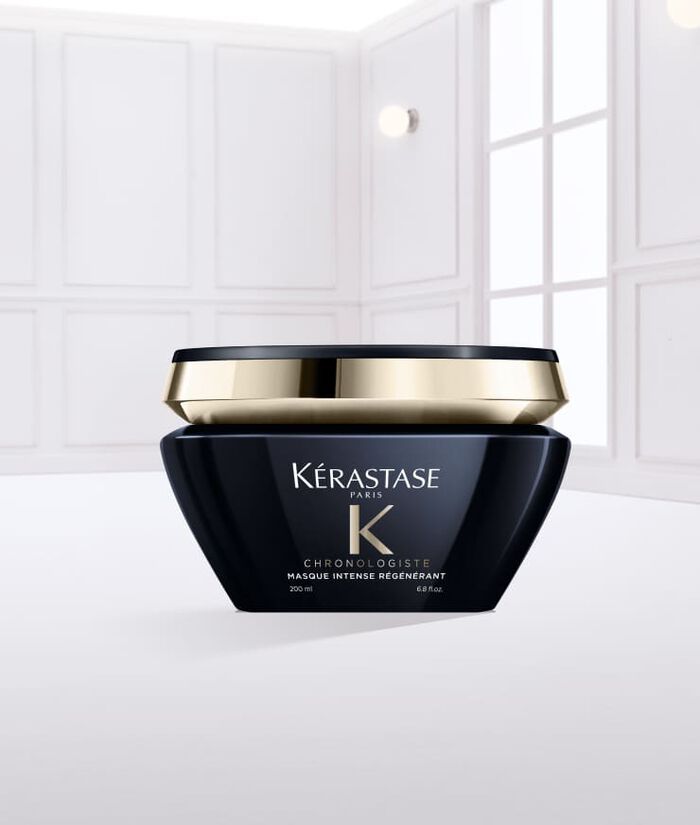 Ein schwarzer Kosmetikbehalter von Kerastase mit goldener Kappe, gefullt mit einer weißen Haarcreme, steht auf einer glatten, weißen Oberflache.