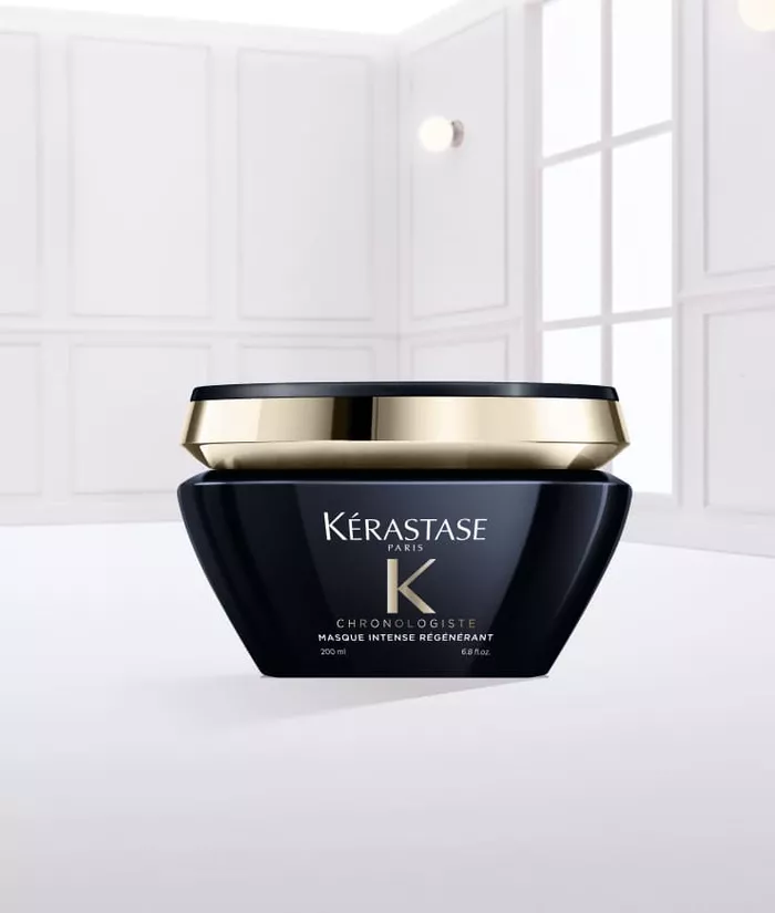 Ein schwarzer Kosmetikbehalter von Kerastase mit goldener Kappe, gefullt mit einer weißen Haarcreme, steht auf einer glatten, weißen Oberflache.