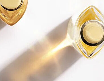 A close-up view of two elegant perfume bottles, one clear and one amber, casting soft shadows on a light background.