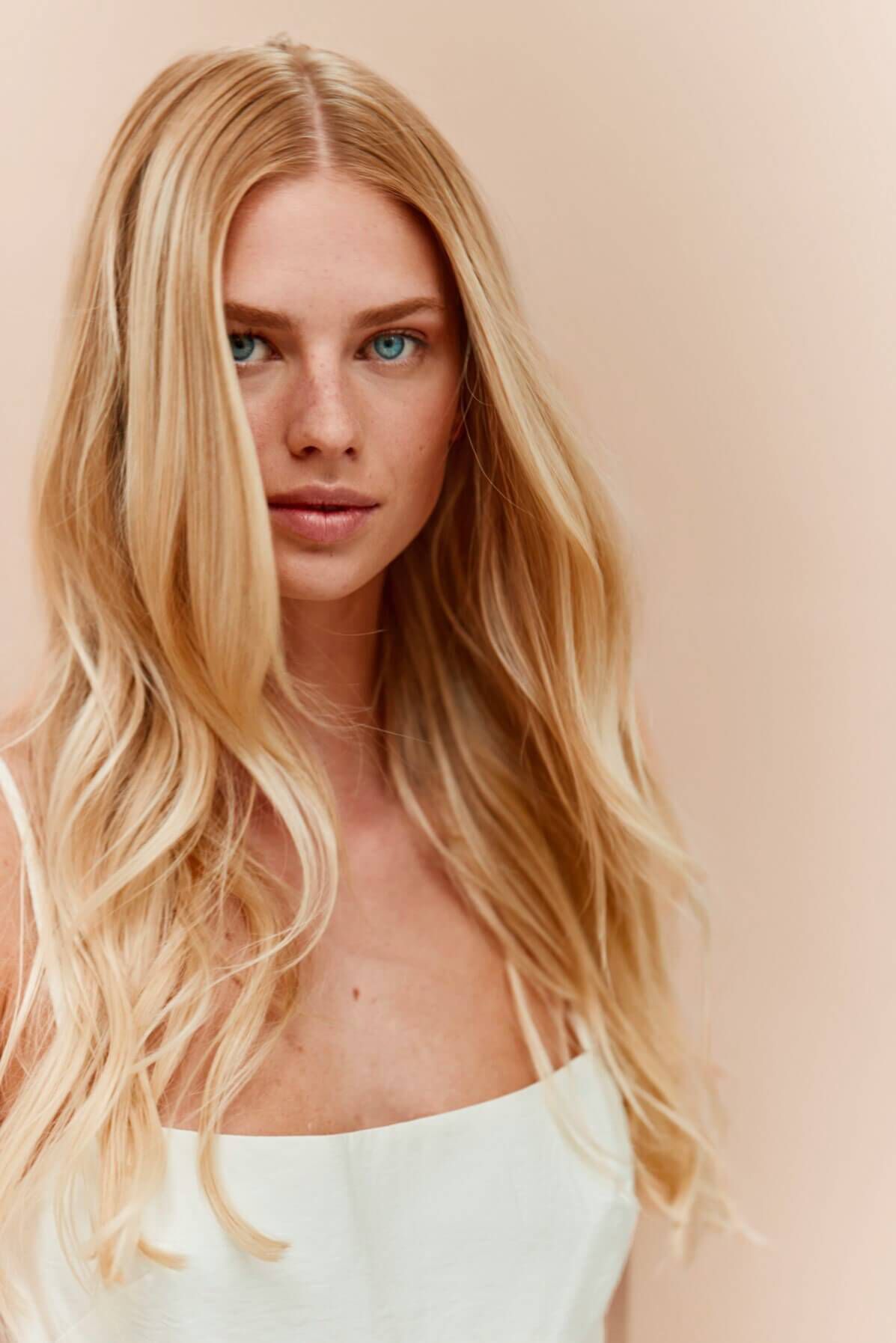 A woman with long, blonde hair and blue eyes looks directly at the camera against a soft, neutral background. She has a natural and serene expression.
