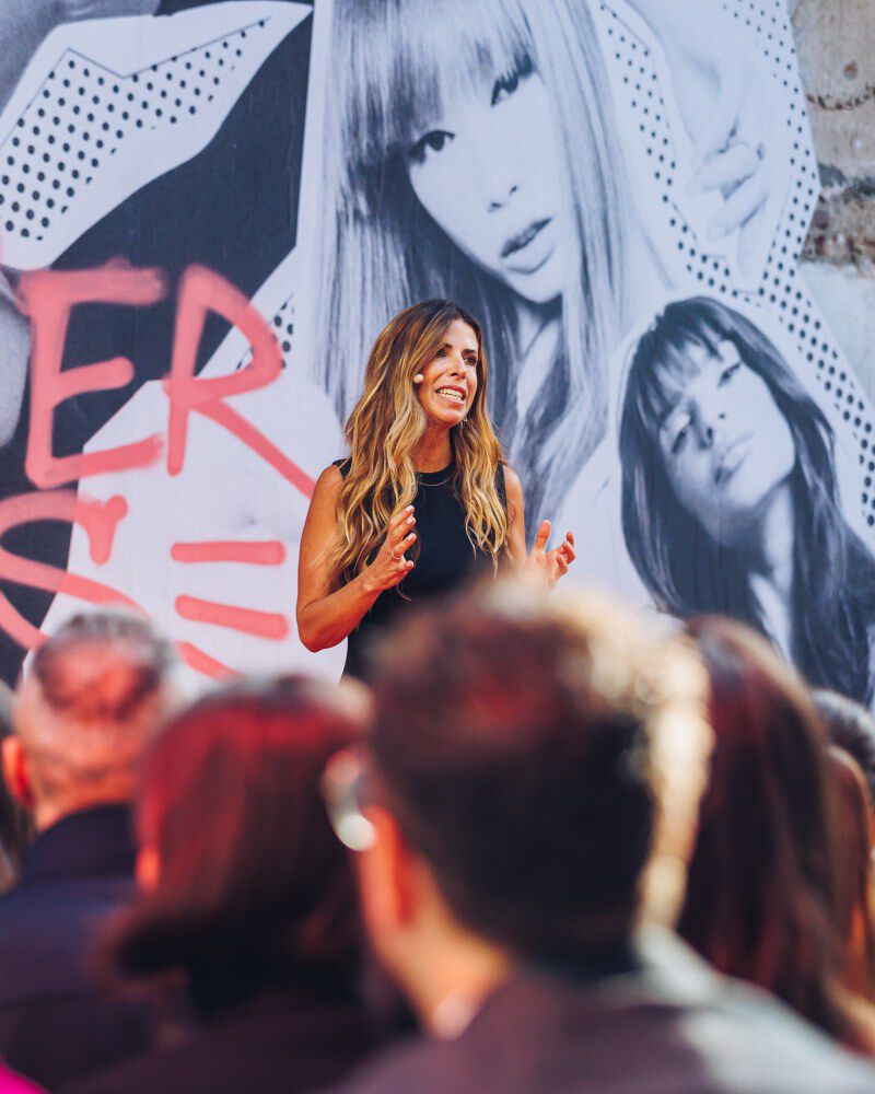 Rosa Carrico, Prasidentin von Kerastase, in einer farbenfrohen Kulisse: blau und rot – mitten in einer Rede am Mikrofon