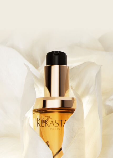 Das Bild zeigt eine Flasche eines Gesichtsserums mit Pipette, eingebettet in eine zarte, blutenahnliche Textur auf hellem Hintergrund.