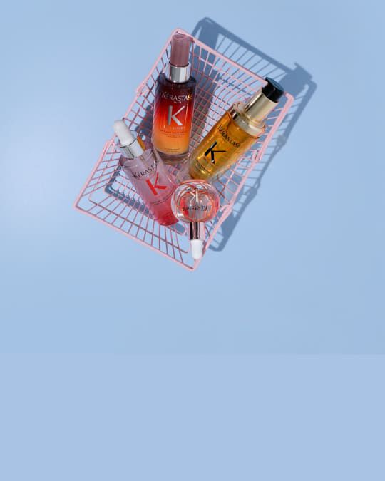 Vier Kerastase Haarpflegeprodukte in rosa Mini-Einkaufswagen auf schwarzem Hintergrund: das Nutritive Serum Nuit 8H, das Elixir Ultime L'Huile Originale, das Serum Anti-chute Fortifiant de Genesis und die Glaze Drops.
