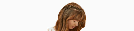 A woman with long, brown hair styled in a half-up, half-down braid, looking downward.