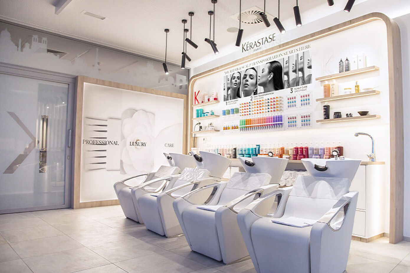 A modern hair salon featuring sleek white shampoo chairs, a well-organized display of hair products on shelves, and bright lighting creating a clean, inviting atmosphere.