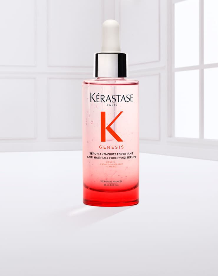 Eine Flasche Kerastase Genesis Haarserum mit Pipette, auf einem hellen Hintergrund, umgeben von einigen Flussigkeitstropfen.