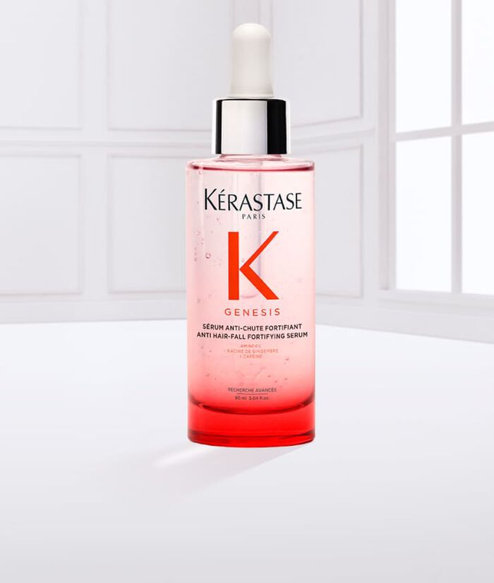 Eine Flasche Kerastase Genesis Haarserum mit Pipette, auf einem hellen Hintergrund, umgeben von einigen Flussigkeitstropfen.