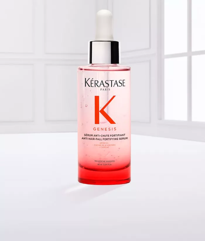 Eine Flasche Kerastase Genesis Haarserum mit Pipette, auf einem hellen Hintergrund, umgeben von einigen Flussigkeitstropfen.