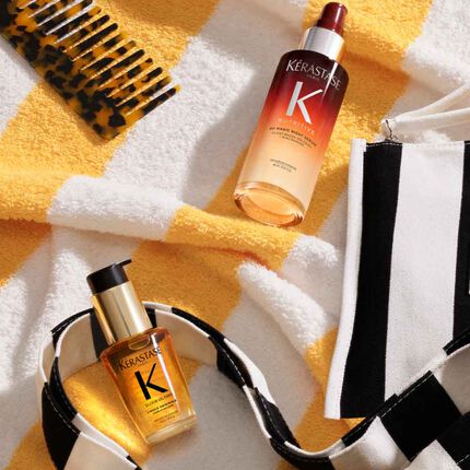Die Kerastase Premiere Produkte liegen auf einem gelb gestreiften Strandtuch, neben dem orange gestreiften Kerastase Taschchen.