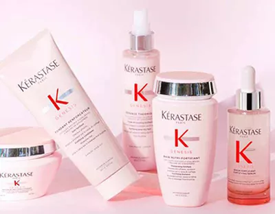 A collection of Kerastase Genesis hair care products displayed on a light pink background, including a shampoo, conditioner, serum, and a restorative mask, all featuring the brand's logo.