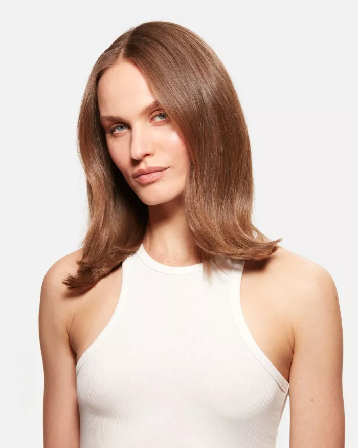 Eine Person mit langen, glatten Haaren und einem neutralen Gesichtsausdruck tragt ein weißes Oberteil.