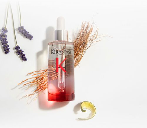 Flasche des Kerastase Genesis Serum Anti-Chute Fortifiant, umgeben von botanischen Elementen wie Lavendel und Ingwer.