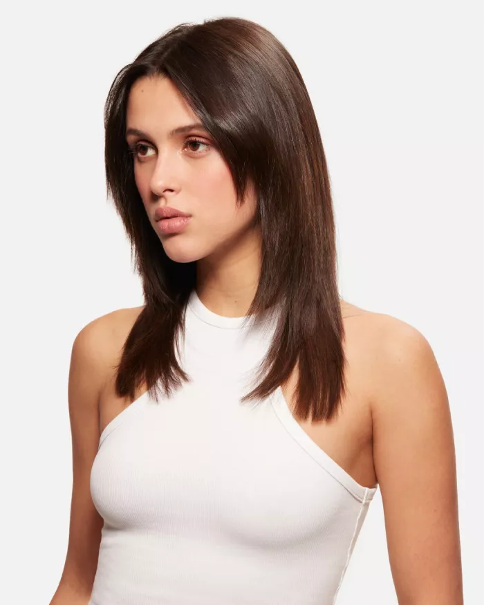 Junge Frau mit langen, glatten Haaren, die in einem weißen Top steht und zur Seite schaut.