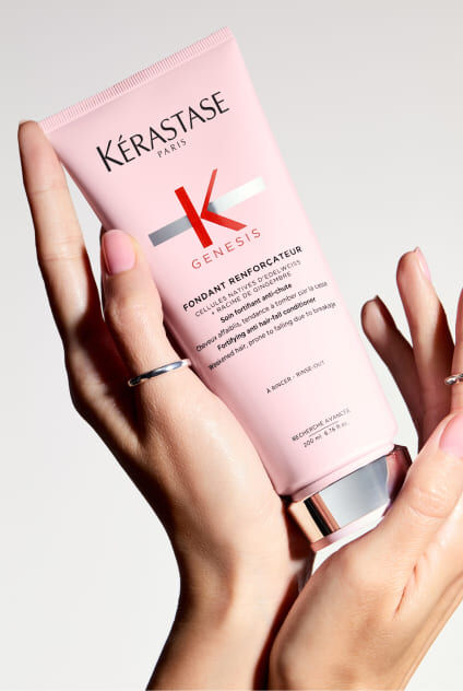 Hande halten eine rosa Tube des Kerastase Genesis Fondant Renforcateur Conditioners.
