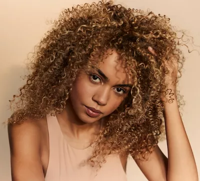 Portrat einer Frau mit lockigem, voluminosem und naturlichem Haar, zur Veranschaulichung der Integration eines Anti-Feuchtigkeits-Produkts in die Haarroutine