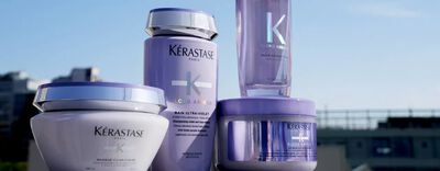 Four Kerastase hair care products in purple containers are displayed against a bright background, featuring labels with the brand name and product details.