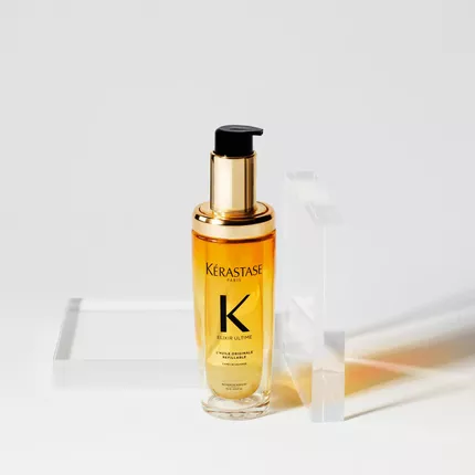 Ein Flakon mit Kerastase Elixir Ultime Haarserum, umgeben von transparenten geometrischen Formen auf einem weißen Hintergrund.