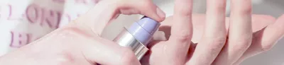 Close-up image of a hand pressing a pump bottle to dispense a creamy product.