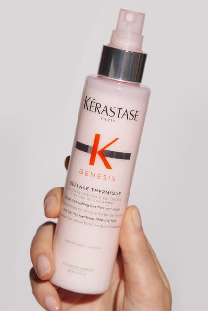 Hand halt eine rosa Flasche Kerastase Genesis Defense Thermique, ein Hitzeschutzspray fur Haare.