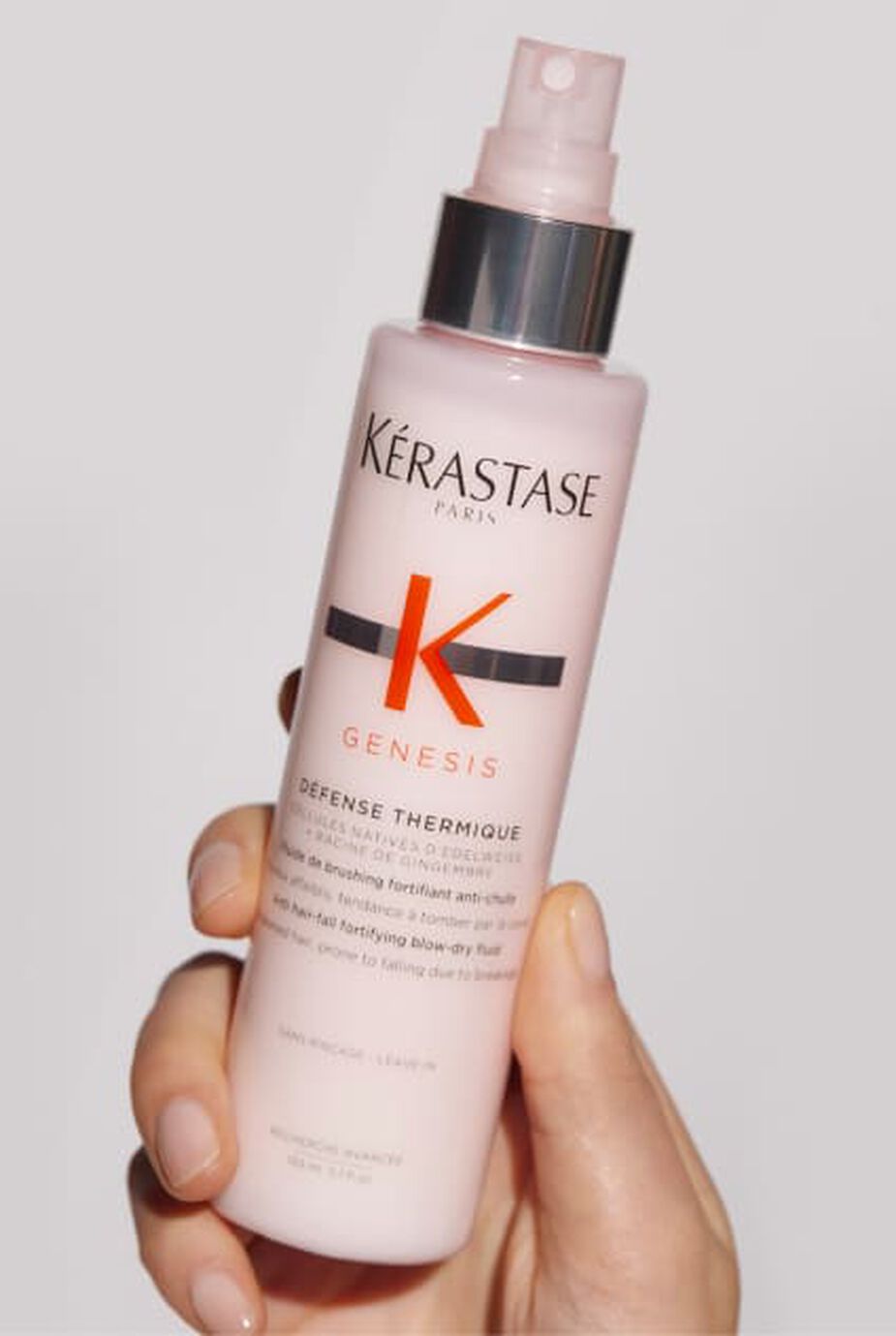 Hand halt eine rosa Flasche Kerastase Genesis Defense Thermique, ein Hitzeschutzspray fur Haare.