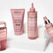 Image of a collection of hair care products displayed on a white pedestal. The products, all in pink packaging, include a shampoo, a hair mask, a leave-in treatment, and a spray.