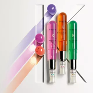 Three colorful skincare serums in bright bottles—pink, orange, and green—are arranged next to graphic, colorful stripes on a white background.