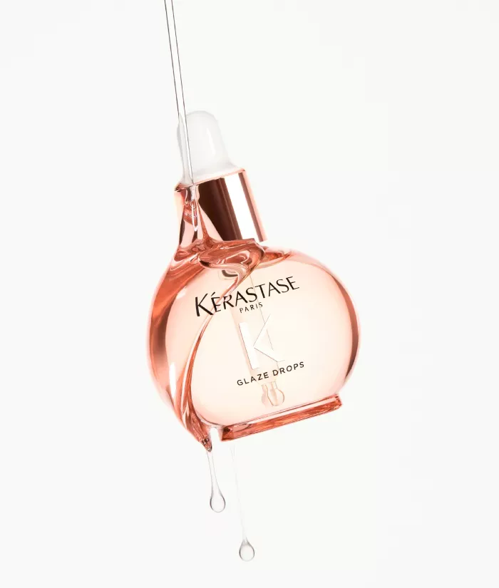 Eine Flasche Kerastase Glaze Drops mit einer tropfenden Pipette, vor einem neutralen Hintergrund.
