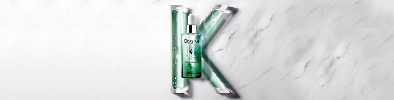 A green bottle of hair serum is displayed at the center, surrounded by flowing green gel tubes on a white marble background, with a stylized letter "K" formed by the arrangement.