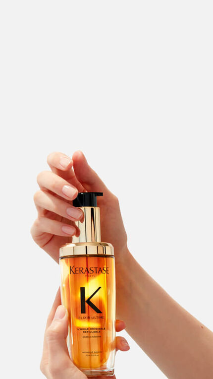 Ein Flakon von Kerastase Elixir Ultime mit goldenem Inhalt, umgeben von spritzenden, goldenen Tropfen.