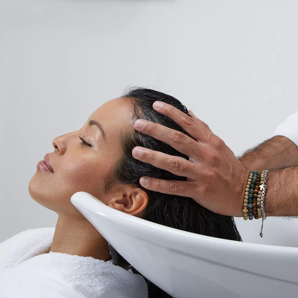 Eine Frau erhalt eine Kopfhautmassage in einem Salon, wahrend sie entspannt im Waschbecken sitzt.