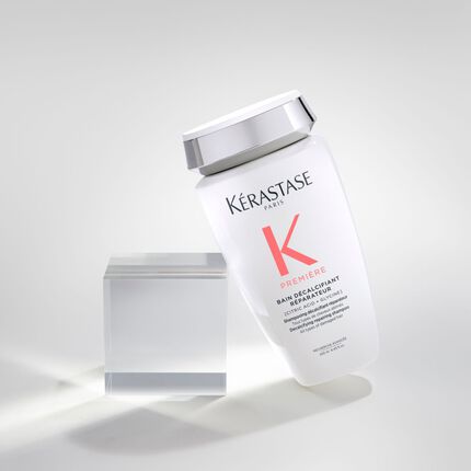 Ein schrag stehender Flakon des Kerastase Premium-Haarshampoos vor einem klaren Block auf einem hellen Hintergrund.