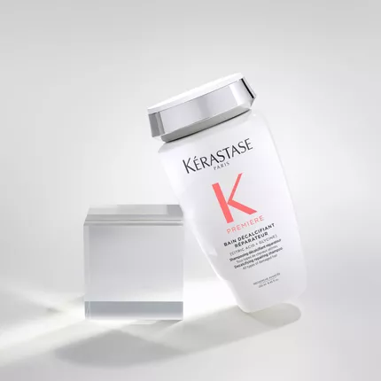 Ein schrag stehender Flakon des Kerastase Premium-Haarshampoos vor einem klaren Block auf einem hellen Hintergrund.