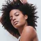 A person with curly hair poses against a light background, showcasing a confident expression.