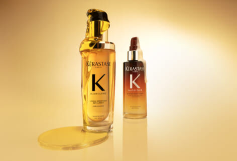 Zwei Kerastase-Produkte, das Elixir Ultime L'Huile Originale (goldene Flasche) und das Nutritive Serum Nuit 8H (Flasche mit orangefarbenem Verlauf), auf golden-gelbem Hintergrund.