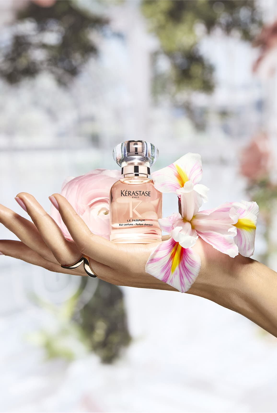Parfum Gloss Absolu, auf einer Hand in einer floralen Umgebung platziert, die an seine Inhaltsstoffe erinnert