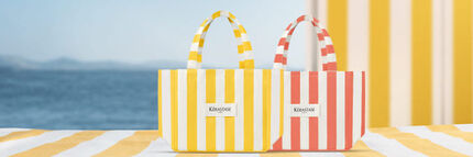 Die Kerastase Produkte Huile Elixir 30ml und Serum de Nuit Nutritive liegen auf einem gelb gestreiften Strandtuch, neben der Tasche und dem schwarz gestreiften Kerastase Taschchen.
