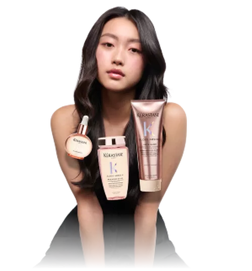 A model with long, dark hair holds hair care products from Kerastase's Gloss Appeal line, including a serum, shampoo, and conditioner, against a transparent background.