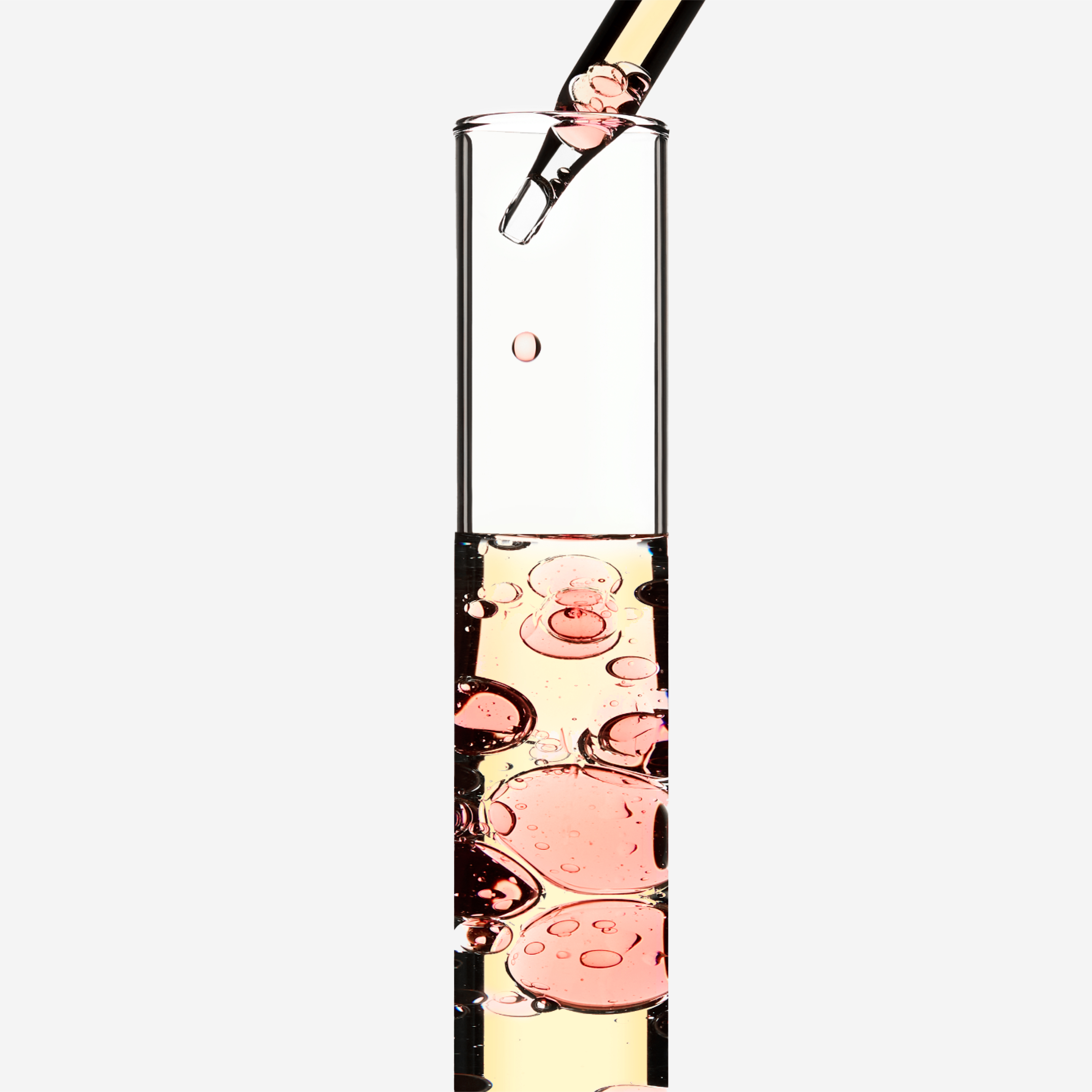 Eine Pipette tropft pinke Flüssigkeit in ein hohes, durchsichtiges Glas mit blasenförmigen Einschlüssen.