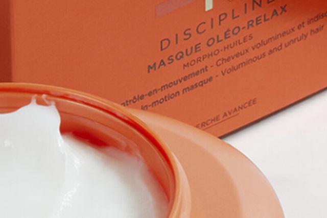 Eine Schale mit weißer Haarmaske, neben einer orangefarbenen Verpackung mit dem Schriftzug 'Discipline'.