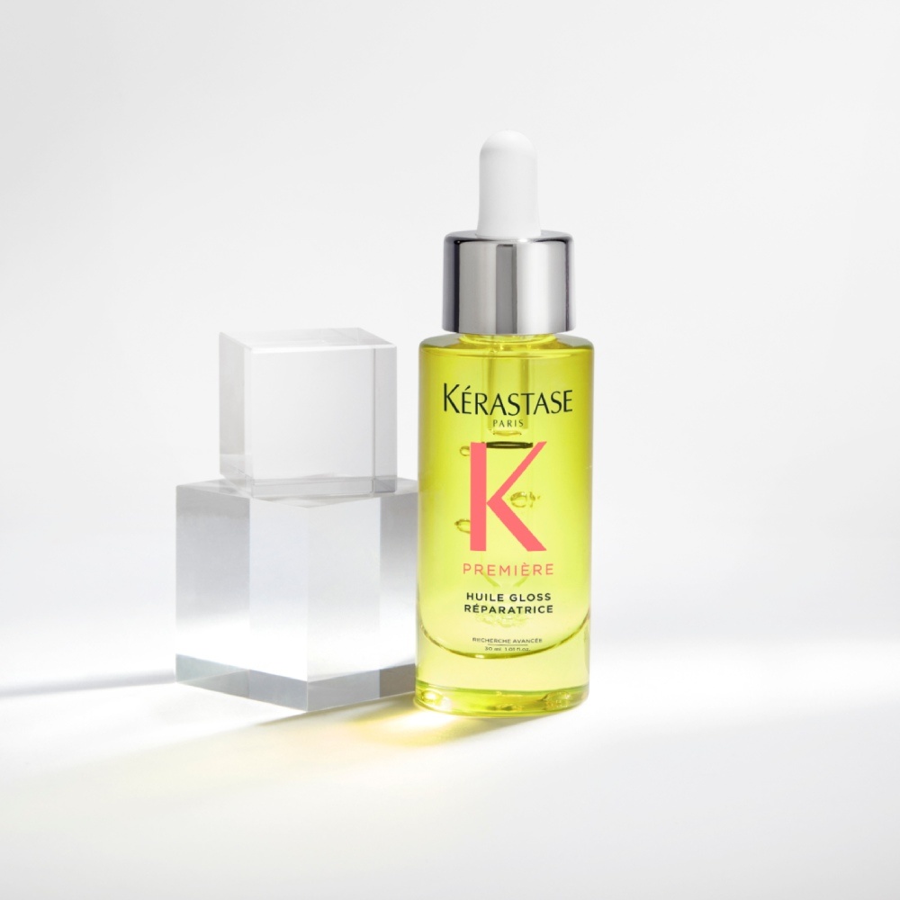 Das Haaröl Première Huile gloss réparatrice wird auf einem rein grauen Hintergrund mit transparenten Würfeln präsentiert. Das Öl verleiht dem Haar Glanz und versiegelt Spliss, gleichzeitig wird stumpfes Haar neutralisiert.