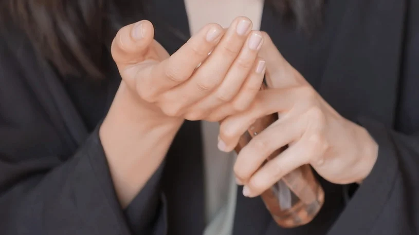 Eine Hand hält eine Flasche, während die andere sanft auf die Finger küsst, um Pflege oder Duft aufzutragen.
