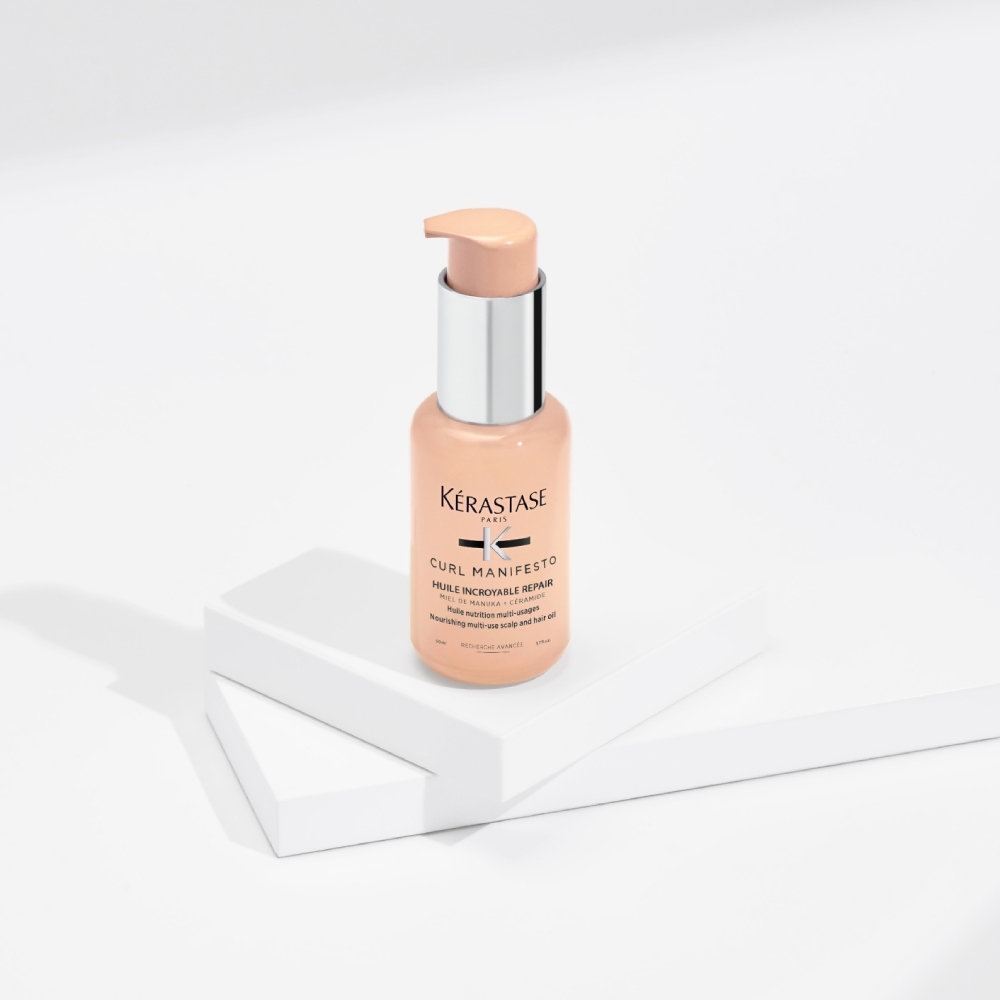Das Haaröl Curl Manifesto Huile Sublime Repair wird auf einem rein grauen Hintergrund mit transparenten Würfeln präsentiert. Dieses Haaröl spendet Feuchtigkeit und definiert die Form von lockigem Haar, gleichzeitig werden Frizz und Haarbruch reduziert.