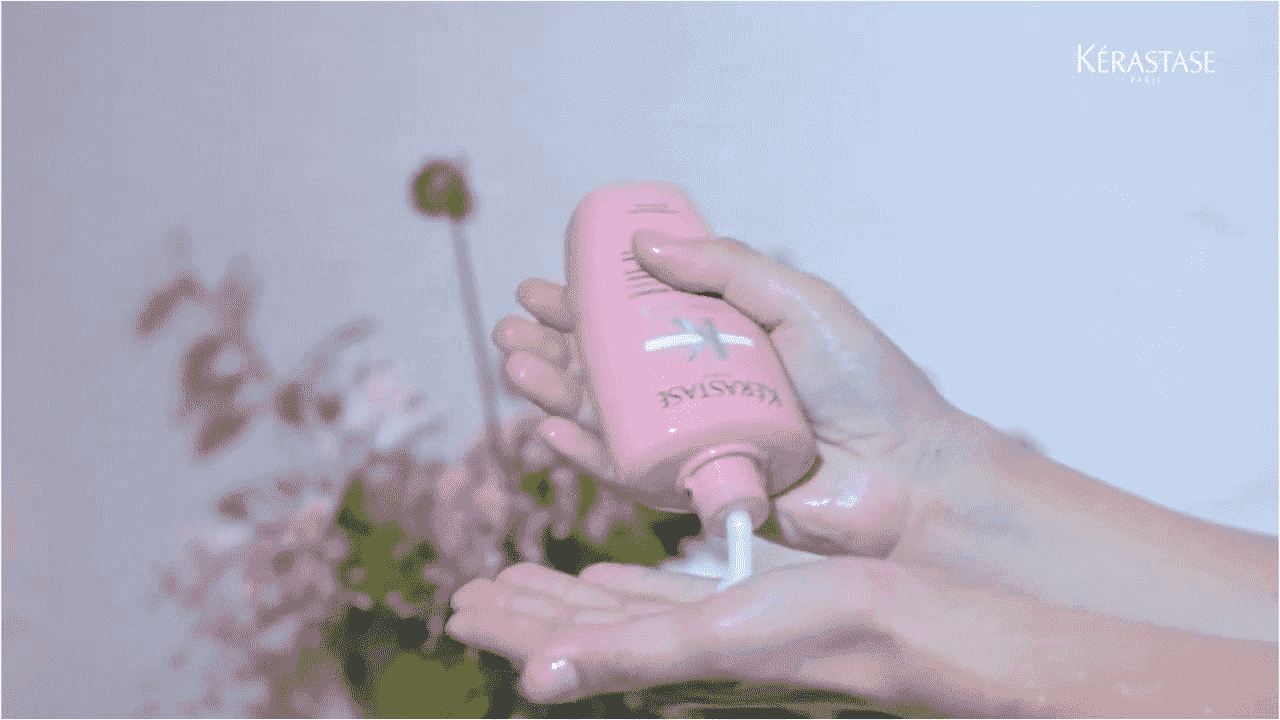 Eine Hand hält eine Flasche Kérastase-Haarpflege, während eine andere Hand Produkt auf die Handfläche gibt.
