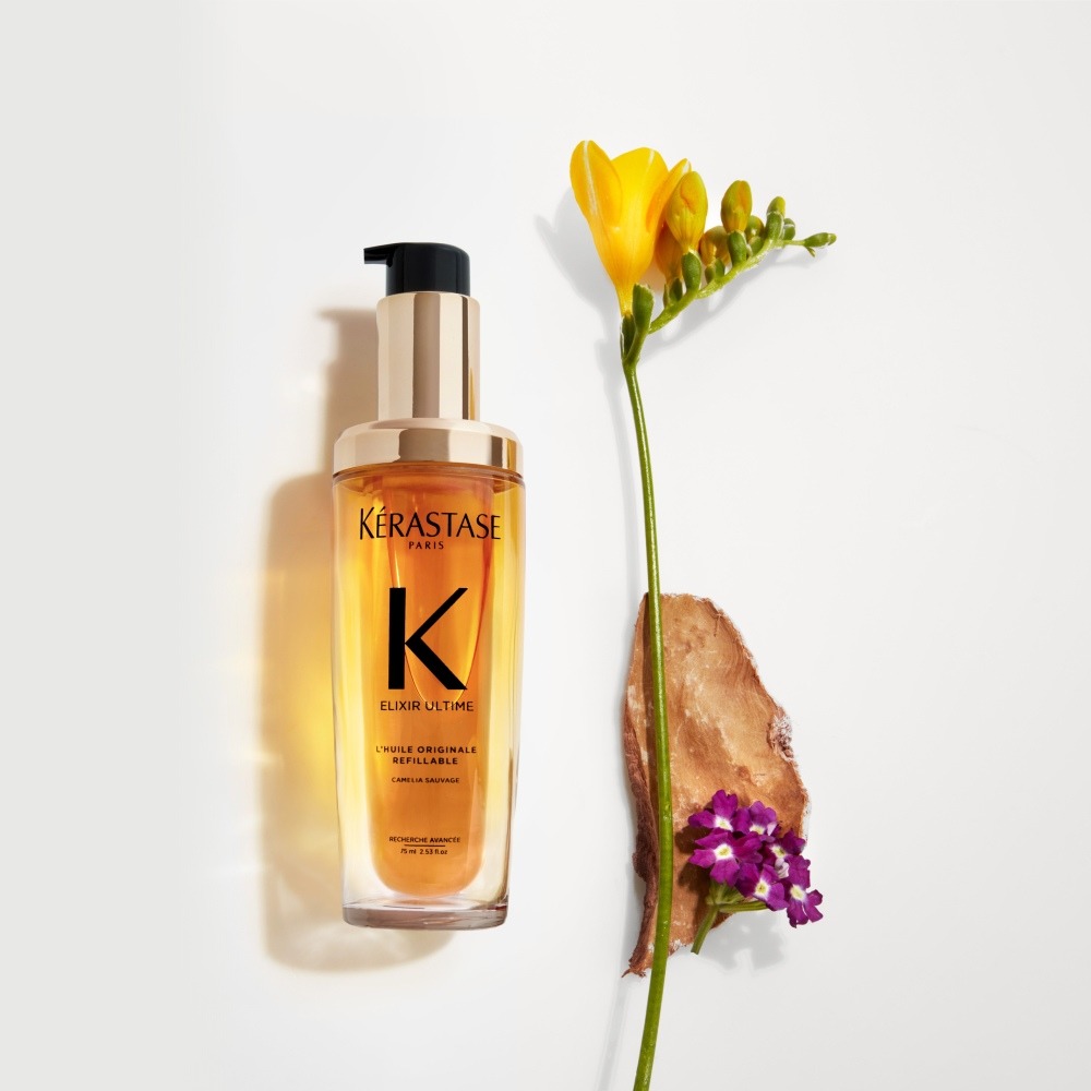 Das neue nachfüllbare Elixir Ultime wird auf einem rein grauen Hintergrund mit Freesien- und Sonnenwendeblüten und Sandelholz präsentiert.